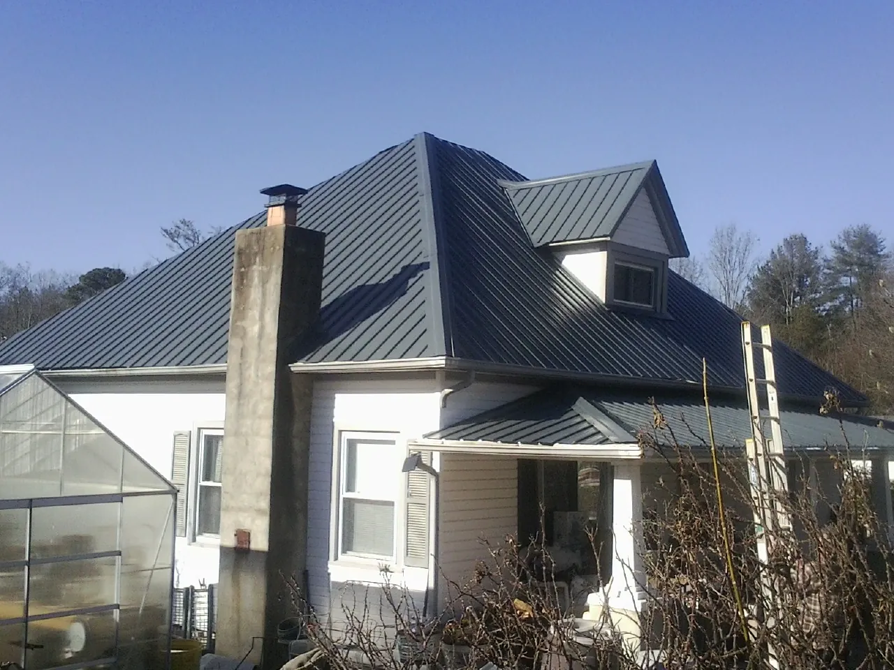 Dark blue standing seam metal roof on a white farmhouse with dormer — Slate & Tile Roof Repair by Roofing Brothers in Manhasset