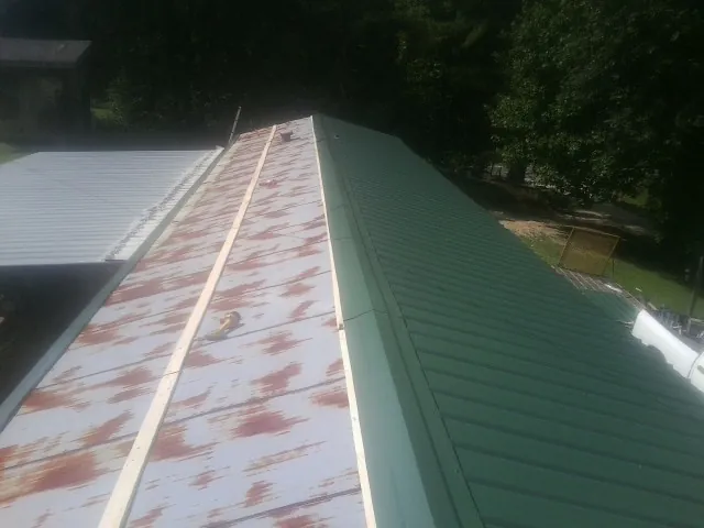 Old rusted panels beside newly installed green metal roofing — Wind Damage Roof Repair by Roofing Brothers in Manhasset