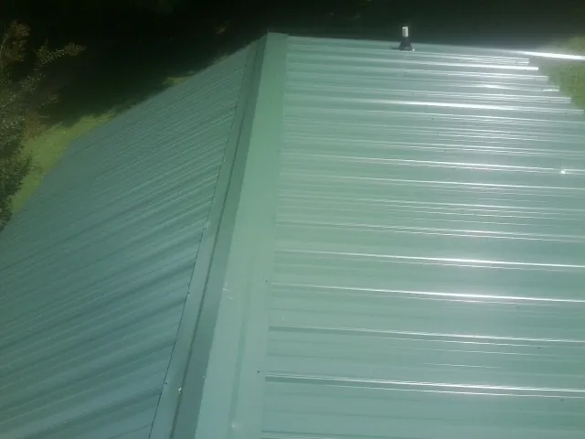 New green metal panels meeting at the ridge of a roof — Flat Roof Repair work by our crew in Manhasset