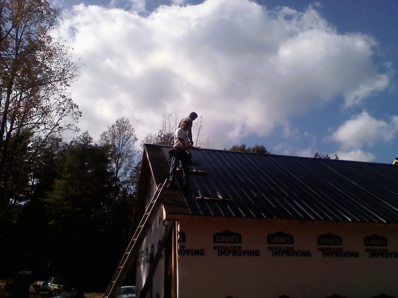 Roofer fastening dark metal panels high against a cloudy sky, from a Roof Inspection job in Manhasset