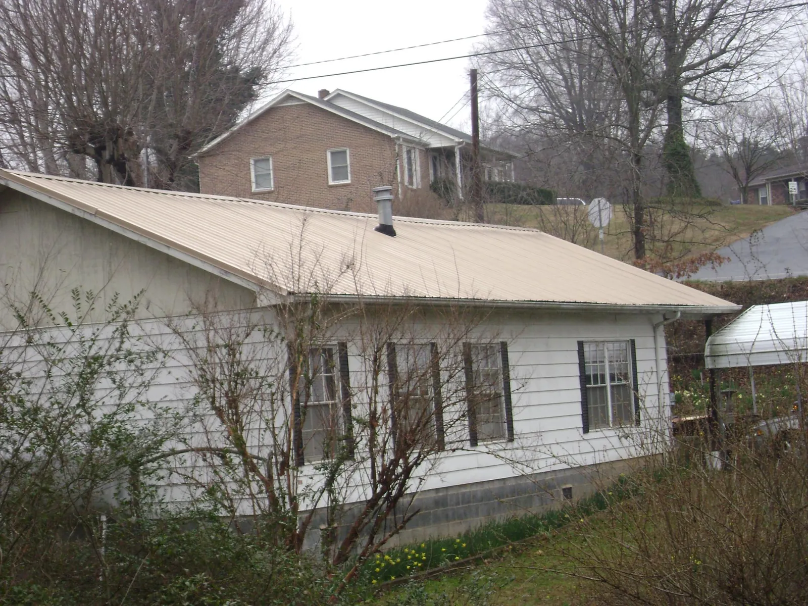 Tan metal roof on a white sided house set into a hillside — Commercial Roofing by Roofing Brothers in Manhasset