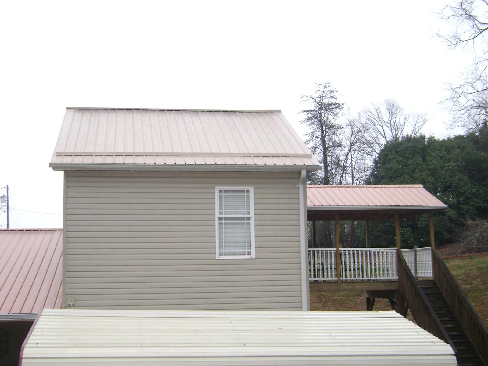 Tan metal roofs on a two story addition and attached porch, from a Roof Replacement job in Manhasset